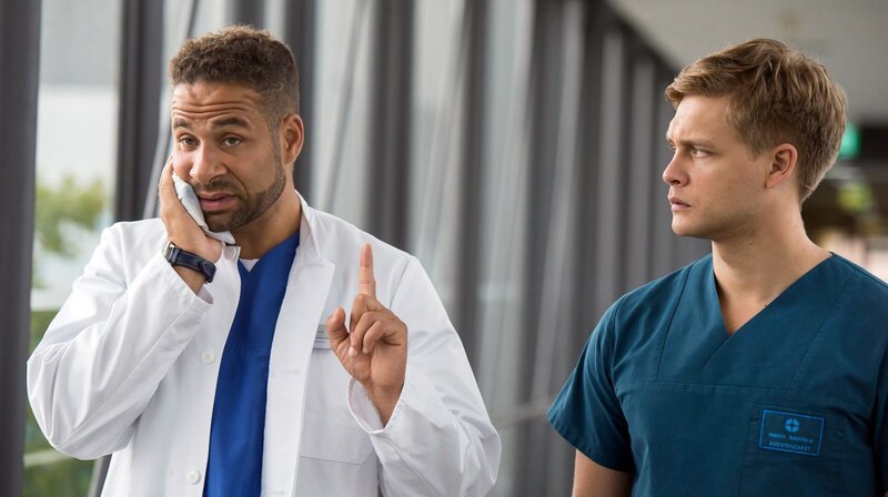 Trotz Schmerzen, behält Dr. Matteo Moreau (Mike Adler, l.) einen kühlen Kopf und weist Mikko (Luan Gummich, r.) auf eine weitere Möglichkeit im Fall Timo hin. – Bild: ARD/​Jens Ulrich Koch
