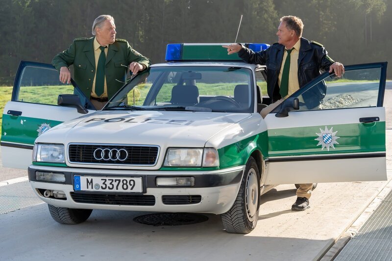 Hubert (Christian Tramitz, r.) und Girwidz (Michael Brandner, l.) fahren mit dem Streifenwagen zum Kieswerk. – Bild: Leonine/​Thomas Neumeier