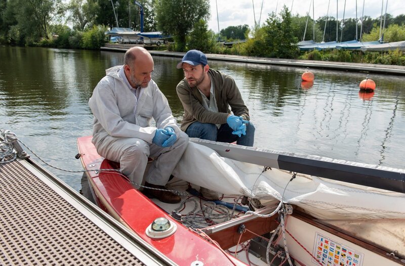 Dr. Henning Strahl (Christoph Tomanek, l.) und Gregor (Jonas Minthe, r.) sitzen in Oliver Bergs Jolle und untersuchen die Blutspuren am Großbaum. – Bild: ARD/​Thorsten Jander