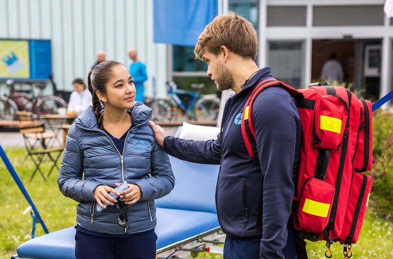 Beim heutigen Spendenlauf des JTK gibt Mikko Rantala (Luan Gummich, r.) alles, um die Teilnehmenden bei Laune zu halten (mit Olivia Papoli-Barawati, l.). – Bild: ARD/​Michael Kremer