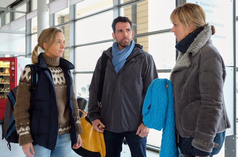 Dr. Lea Peters (Anja Nejarri, re.) wird zu Arbeitsbeginn von ihrem ehemaligen Patienten Lutz Kleinschmidt (Thomas Bartling, mi.) und seiner Frau Nora (Johanna Klante, li.) überrascht. Lutz war vor etwa zwei Jahren in der Sachsenklinik, da er eine Bandwurmzyste im Hirn hat. Lutz und Nora hatten sich damals gegen eine OP entschieden, da sie mit dem Fahrrad die Welt umrunden wollten. Nun sind sie zurück und wollten die Zyste von Dr. Peters entfernen lassen. – Bild: Sebastian Kiss