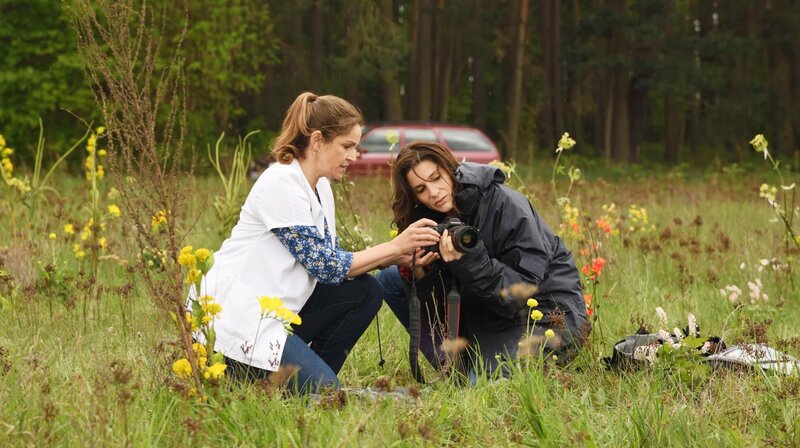 Vera (Rebecca Immanuel) versucht Franziska Loer (Christina Hecke) bei dem Versuch zu helfen, für einen Fotokalender Blumen zu fotografieren.. – Bild: ARD Degeto/​Hardy Spitz
