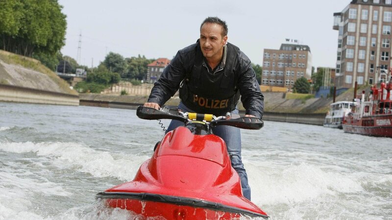Semir (Erdogan Atalay) nimmt mit einem Jet-Ski die Verfolgung Mahlers auf, der mit einem Boot flüchten will. – Bild: MG RTL D /​ Guido Engels