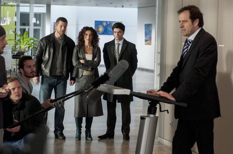 Als Pressesprecher der Polizei gerät Ferchert (Helmfried von Lüttichau, r.) schon bald kräftig ins Visier der Lokalreporter. Um diese zu besänftigen, gründet er ad hoc die Soko „Wurst“. Tanja (Proschat Madani, 3.v.r.), Mick (Henning Baum, 4.v.r.) und Andreas (Maximilian Grill, 2.v.r.) zweifeln an seinem Verstand … – Bild: SAT.1 /​ Martin Rottenkolber