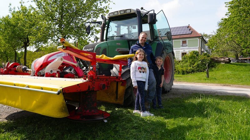 Bernhard Hauer (Mitte) mit zwei seiner vier Kinder und seinem Traktor vor dem familieneigenen Vierkanter. – Bild: ServusTV /​ DMG Film
