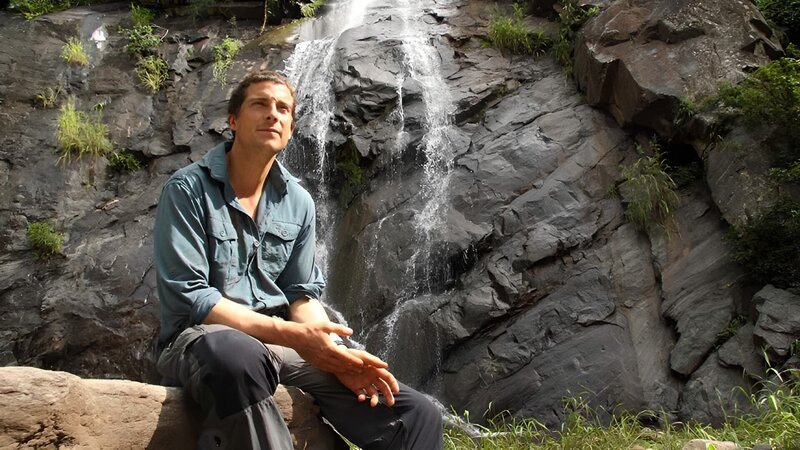 Portrait of Bear Grylls in front of waterfall in Zambia. – Bild: Warner Bros. Discovery