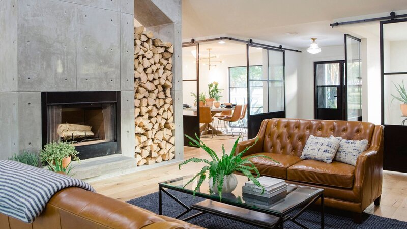 As seen on Fixer Upper, the living room in the Wixsom’s remodeled house has new hardwood floors, concrete walls and a fireplace that separates the kitchen from the living room. – Bild: HGTV/​Scripps Networks, LLC.