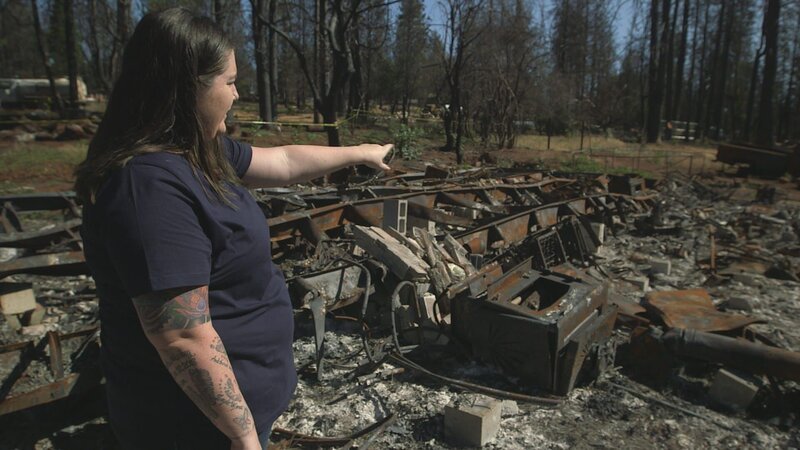 Anastasia zeigt auf das, was von ihrem Haus nach dem Waldbrand übrig geblieben ist. – Bild: MMXIX Weather (OHM) Productions Inc.