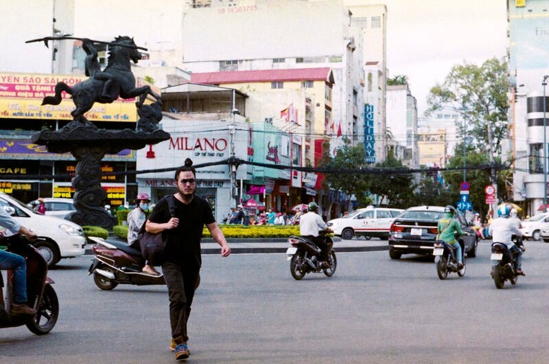 Host Robert Joe crosses a busy street in Ho Chi Minh City. – Bild: National Geographic Channels/​Jeanette Lim