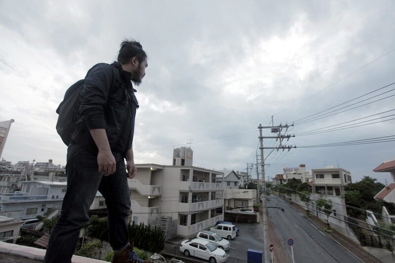 Robert Joe überblickt eine Straße in Okinawa vom Dach des Crown Hotels aus. – Bild: PLURIMEDIA (National Geographic Channels /​ Dominic Young)