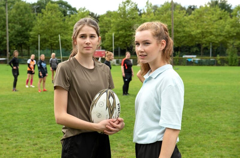 Vanessa Schübel (Marleen Quentin, l.) und Lea Jansen (Louisa Kruse, r.) bemerken, dass ihnen auch ungebetene Gäste beim Rugby zusehen (mit Kompars:innen, h.). – Bild: ARD/​Thorsten Jander