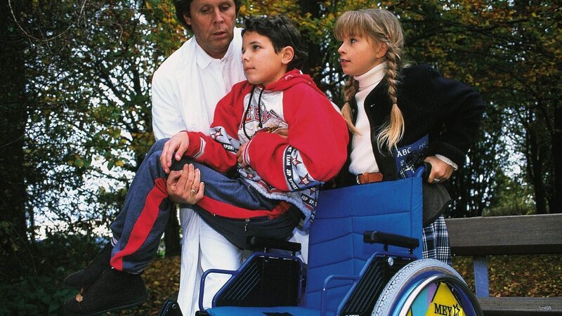 Iris (Jana Kilka) besucht ihren neuen Freund Manuel (David Lütgenhorst) im Krankenhaus. Dr. Stefan Frank (Sigmar Solbach, l.) packt den kleinen Patienten in den Rollstuhl. – Bild: MG RTL D /​ Elke Werner