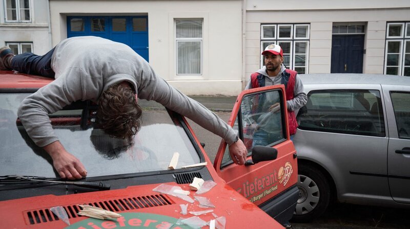 In der Lübecker Altstadt ist ein Mann aus dem Fenster gestoßen worden und landet auf dem Auto eines Fast-Food-Lieferanten. – Bild: ARD/​Georges Pauly