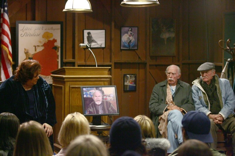 Da Taylor (Michael Winters, M.) nicht selbst anwesend sein kann, leitet er die Stars Hollow Stadtversammlung via Bildschirm … – Bild: Warner Brother International Television Lizenzbild frei