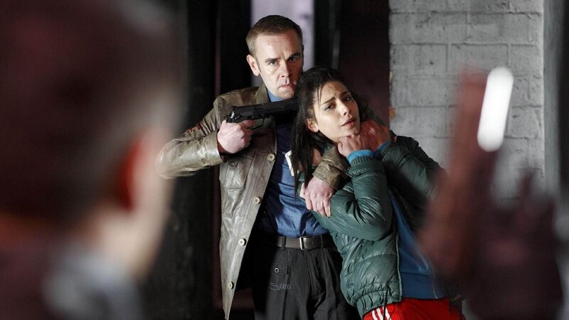 Ziegler (Frank Giering, hinten l.) hat Shirin (Nadia Hilker) in seiner Gewalt und droht Semir (Erdogan Atalay, Rückansicht) seine Geisel zu erschießen. – Bild: TVNOW /​ Guido Engels