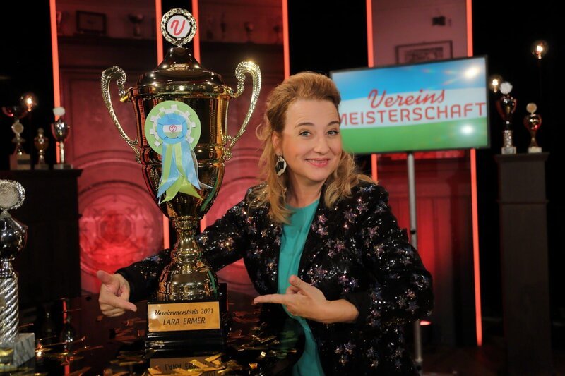 „Vereinsmeisterschaft“ das große Finale: In der diesjährigen Staffel Vereinsheim Schwabing bekamen neue Talente die Chance, ihr Können unter Beweis zu stellen. In den vergangenen vier Wochen hatte nun die Jury die Aufgabe, die Auftritte der acht Kandidaten und Kandidatinnen zu bewerten und sich zu einigen, wer das Zeug zur Vereinsmeisterin oder zum Vereinsmeister hat. Das Ergebnis wird heute feierlich durch Jury-Chef Hannes Ringlstetter an Moderatorin Constanze Linder (im Bild) übergeben. – Bild: BR/​Foto Sessner/​Foto Sessner