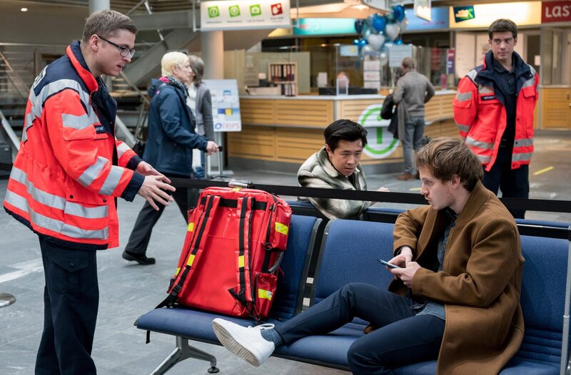 Die Streithähne Nick Jauer (Xidou Zhao) und Marvin Verl (Joscha Eißen) sitzen am Flughafen fest und werden von Ben Ahlbeck (Philipp Danne) und Elias Bähr (Stefan Ruppe) versorgt. – Bild: ARD/​Jens-Ulrich Koch