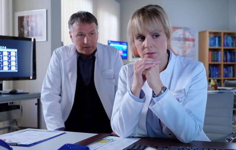 Dr. Lea Peters informiert Klinikleiter Dr. Roland Heilmann darüber, dass bei einem kleinen Patienten Kindesmisshandlungen vorliegen könnte. Lea ist sich sogar so sicher, dass sie das Jugendamt informieren will. Dr. Heilmann bittet Lea, vorerst die Ergebnisse der weiteren Diagnostik abzuwarten. Ihr Verdacht ist gravierend und damit ist nicht leichtfertig umzugehen – doch das tut Lea auch nicht. – Bild: BR/​MDR/​Saxonia Media Filmproduktions GmbH/​Sebastian Kiss