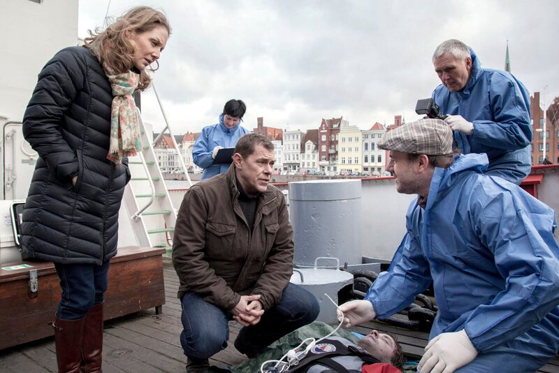 Die Besatzung eines Feuerwehrschiffs (Komparsen) hat einen Toten aus dem Wasser gezogen. Pathologe Dr. Strahl (Christoph Tomanek, r.) erklärt Finn (Sven Martinek, M.) und Elke Rasmussen (Tessa Mittelstaedt, l.), dass es kein Unfall war, sondern dass es sich um Mord handelt: an einem Sicherungsseil wurde manipuliert. – Bild: NDR/​ARD/​Georges Pauly
