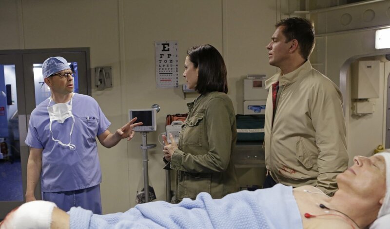 Nachdem Gibbs (Mark Harmon, liegend) angeschossen wurde, machen sich CIA Officer Joanna Teague (Mimi Rogers, M.) und DiNozzo (Michael Weatherly, r.) großen Sorgen um ihn. Doch Dr. Cyril Taft (Jon Cryer, l.) gibt alles, um ihn zu retten … – Bild: CBS Television /​ Sonja Flemming