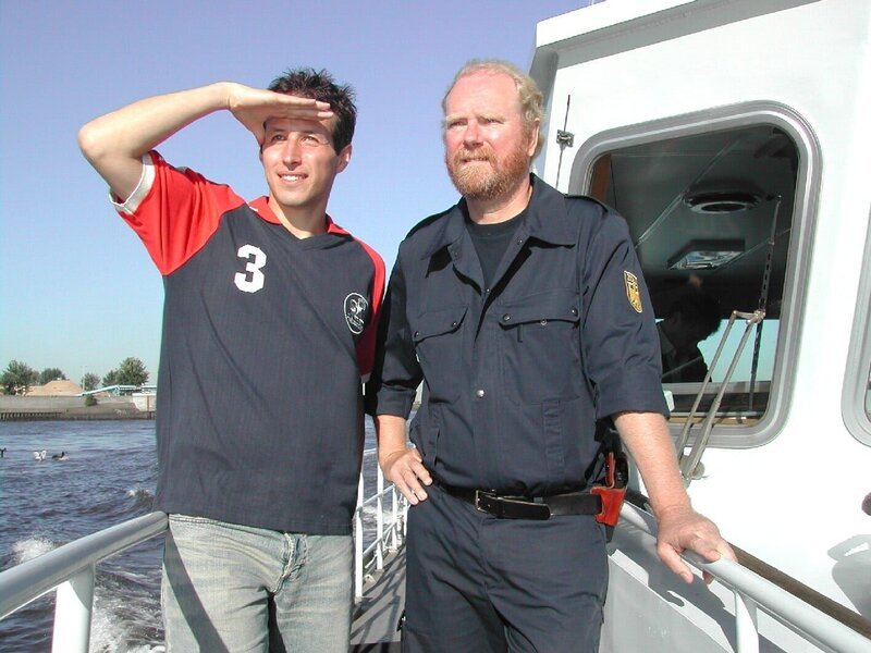 Willi Weitzel mit einem Zollbeamten auf dem Zollschiff im Hamburger Hafen. Mit ihnen ist Willi unterwegs, um einen Bananenfrachter aus Kolumbien auf Schmuggelware zu durchsuchen. – Bild: BR/​megaherz gmbh