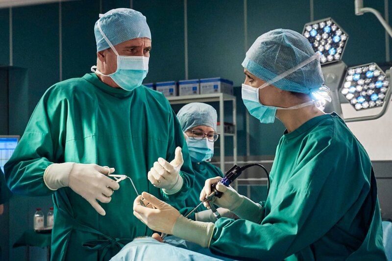 Der renommierte Schweizer Neurochirurg Dario Brosi (Markus Böker, li.) kommt an die Sachsenklinik, um zu demonstrieren, wie man eine Hypophysen-OP schneller und effektiver durchführt. Als Assistenz an seiner Seite, steht Dr. Lea Peters (Anja Nejarri, re.), seine ehemals beste Studentin an der Uni in Zürich. Brosi erweist sich bei der OP als genauso gut, wie sein Ruf, bis ihn ein Krampf in der Hand dazu zwingt die OP an Lea abzugeben. – Bild: MDR/​Saxonia/​Wernicke