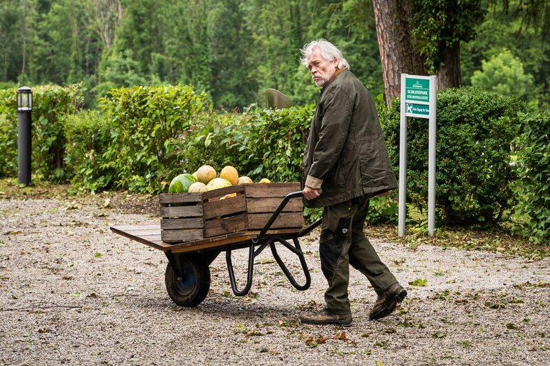 Als Hubert und Girwidz am Hotel ankommen, begegnet ihnen ein ominöser Gärtner (Klaus Stiglmeier) mit einer Schubkarre voll Obst – Bild: Leonine