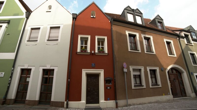 Das kleinste Hotel der Welt (rotes Haus) von außen. – Bild: BR/​south & browse GmbH/​Susanne Noack