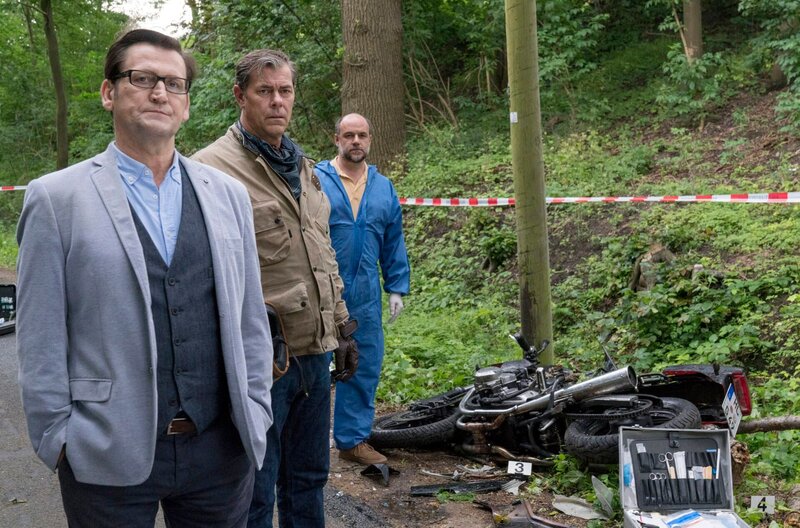 Als die Spurensicherung ermittelt, dass der Motorradfahrer Opfer eines perfiden Anschlags wurde, werden Lars (Ingo Naujoks, l.), Finn (Sven Martinek, 2.v.l.) und Dr. Strahl (Christoph Tomanek, r.) in die Ermittlungen eingeschaltet. – Bild: WDR/​ARD/​Georges Pauly