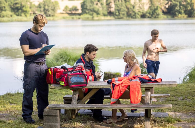 Dr. Mikko Rantala (Luan Gummich, l.) und Florian Osterwald (Lion Wasczyk, 2.v.l.) helfen einer Notfallpatientin am See (mit Kompase, h.). – Bild: ARD/​Michael Kremer