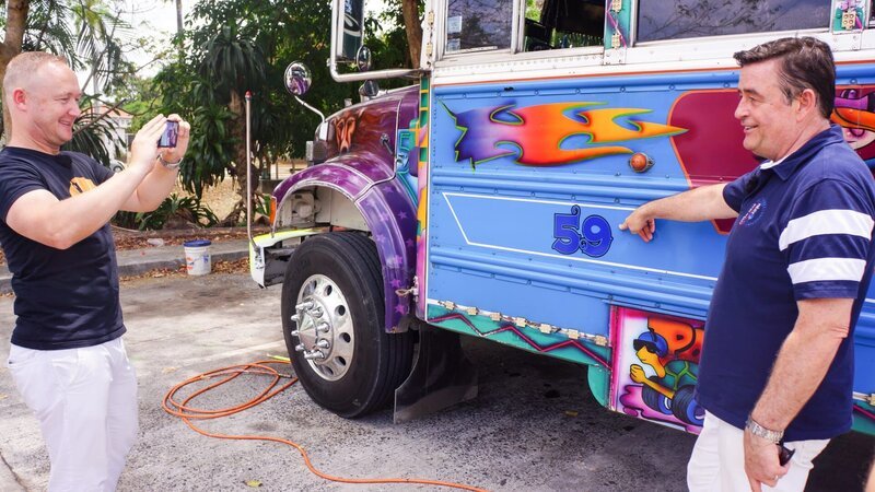 Reiseleiter Bernd und Kreuzfahrtdirektor Thomas Gleiß (rechts) fahren mit einem bemalten Oldtimer-Schulbus durch Panama City. Thomas Gleiß lässt sich von Bernd mit dem Bus fotografieren. – Bild: Bewegte Zeiten Filmproduktion GmbH/​BR/​Deborah Stöckle