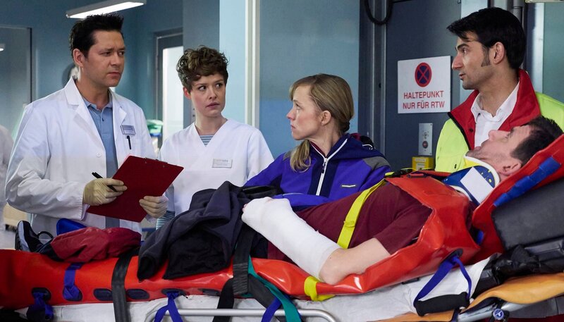 Auf der letzten Testfahrt vor ihrer Weltumrundung per Rad, hatten Nora (Johanna Klante, mi.) und Lutz Kleinschmidt (Thomas Bartling, liegend) einen Unfall. Der Notarzt (Roman Petermann, re.) übergibt die beiden in der Sachsenklinik an Dr. Philipp Brentano (Thomas Koch, li.) und Schwester Svenja Werth (Laura Louisa Garde, 2.v.li.). – Bild: MDR/​Saxonia/​Wernicke