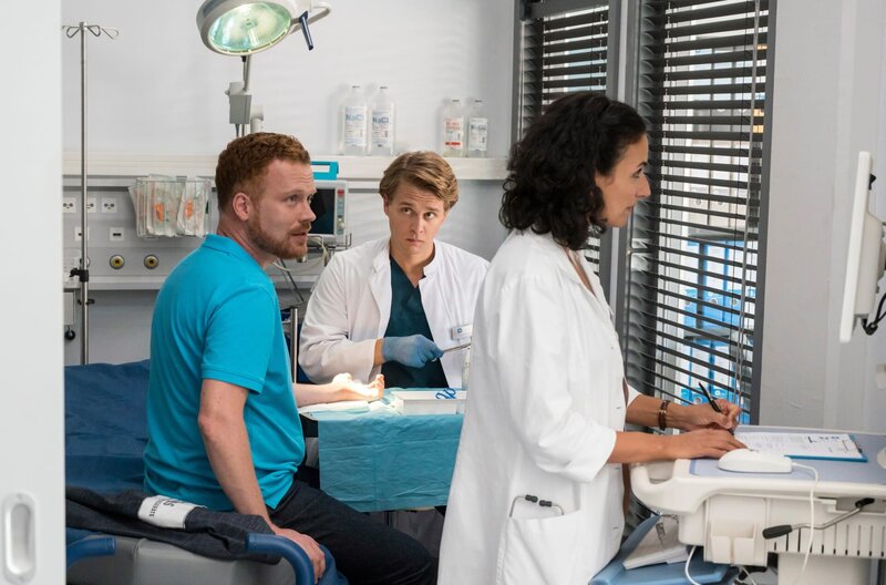 Mikko Rantala (Luan Gummich) und Leyla Sherbaz (Sanam Afrashteh) versorgen eine Schnittverletzung, die sich Jörg Zimpher (Florian Hacke, l.) beim Aufbauen eines Gerätes im Physioraum zugezogen hat. – Bild: ARD/​Jens Ulrich Koch