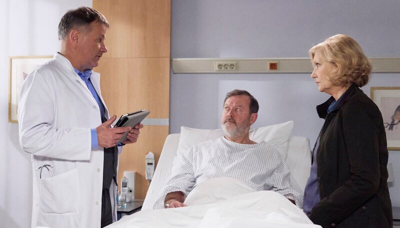 Rainer Heitz (Wolfgang Häntsch, mi.) benötigt laut Dr. Peters ein neues Hüftgelenk. Bärbel Heitz (Rita Feldmeier, re.), eine erfahrene Physiotherapeutin, forderte eine zweite Meinung. Doch Dr. Roland Heilmann (Thomas Rühmann, li.) stimmt mit Dr. Peters überein. Bei Rainers Befund, ist eine Endoprothese die einzig vernünftige Entscheidung. – Bild: MDR/​Saxonia/​Wernicke