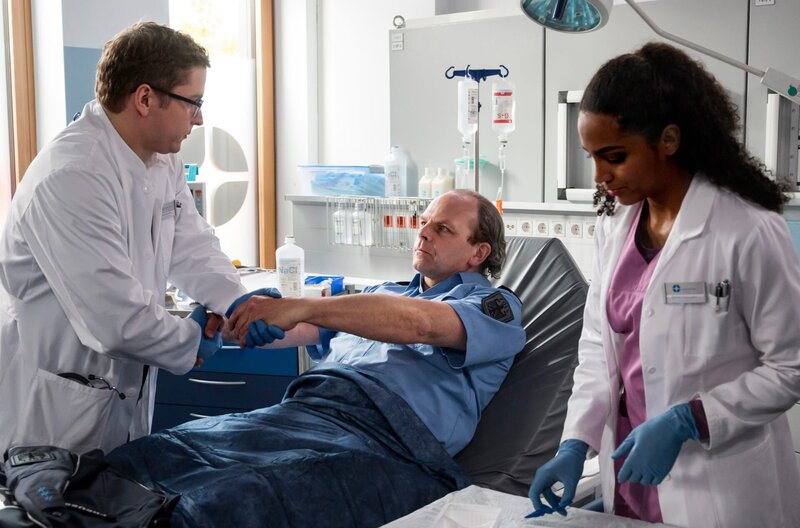 Elias Bähr (Stefan Ruppe, l.) und Emma Jahn (Elisa Agbaglah, r.) untersuchen den Zollfahnder Volker Preuss (Andreas Schröders, M.). – Bild: ARD/​Jens Ulrich Koch