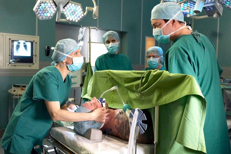 Adrian Walter (Marko Dyrlich, liegend) hat nach seinem Fahrradunfall schwerste Verletzungen. Während der OP kommt es zu Komplikationen. Dr. Kathrin Globisch (Andrea Kathrin Loewig, li.) bittet Dr. Philipp Brentano (Thomas Koch, re.) zu unterbrechen. Als es sogar zum Herzstillstand kommt und Kathrin den Defibrillator ansetzen will, traut sie ihren Augen nicht: Adrian ist wach! Mitte: zwei Komparsen – Bild: MDR/​Saxonia/​Wernicke