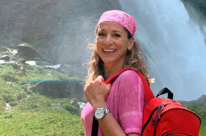 Tamina Kallert am Ufer der Krimmler Ache vor Österreichs höchsten Wasserfällen, die Krimmler Wasserfälle. – Bild: WDR/​Bavaria Entertainment GmbH/​Christine Hiss