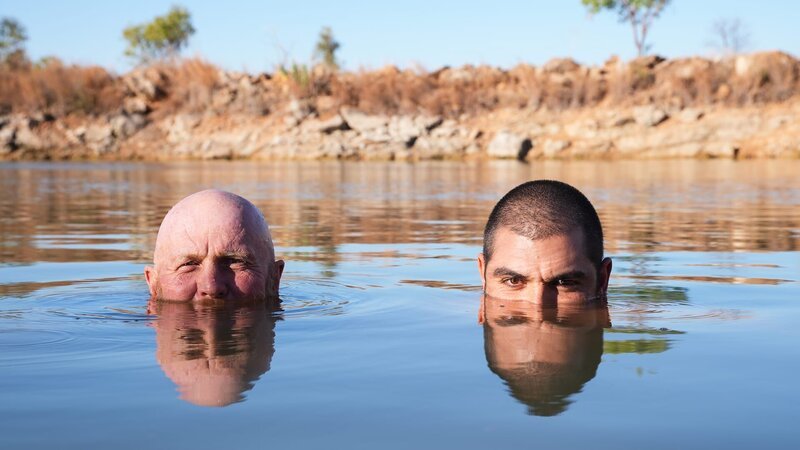 Rod Manning [left] and James „JC“ Caruana [right] swimming in a lake with the outback behind them, both looking at the camera, in Western Australia. – Bild: Warner Bros. Discovery, Inc. or its subsidiaries and affiliates