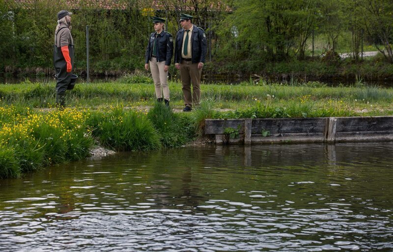 Alois Sailer (Stephan Zinner) wird befragt. Hat er als Fischzüchter Jagd auf Kormorane gemacht? (Mitsou Jung als Christina Bayer, m.; Paul Sedlmeir als Martin Riedl, r.) – Bild: Leonine /​ Kai Neunert