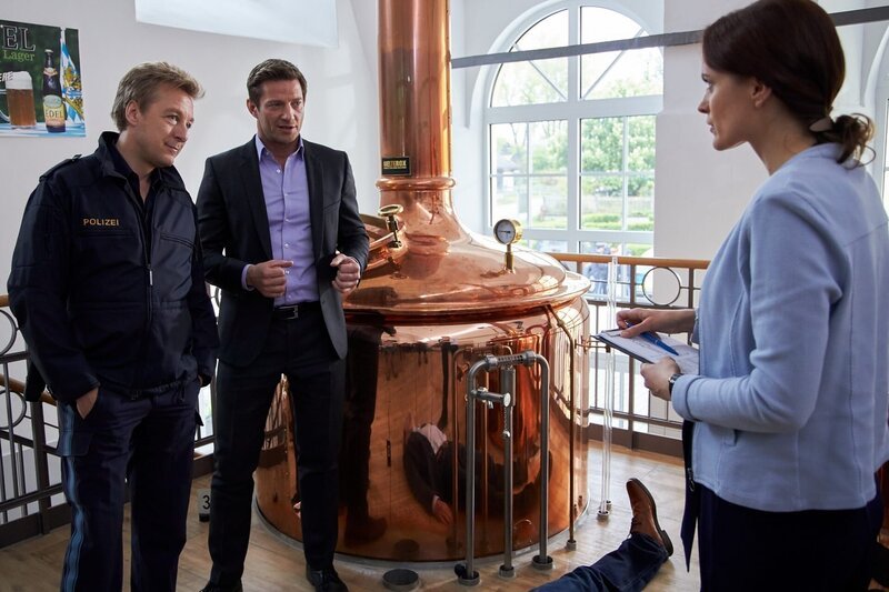 Der Chef der Firma „Bartlbräu“ wurde tot in seiner eigenen Brauerei aufgefunden. Pathologin Mai (Sina Wilke) klärt Kommissar Hansen (Igor Jeftic) und Polizeihauptmeister Mohr (Max Müller) über die Todesursache auf. – Bild: ORF/​ZDF/​Bojan Ritan