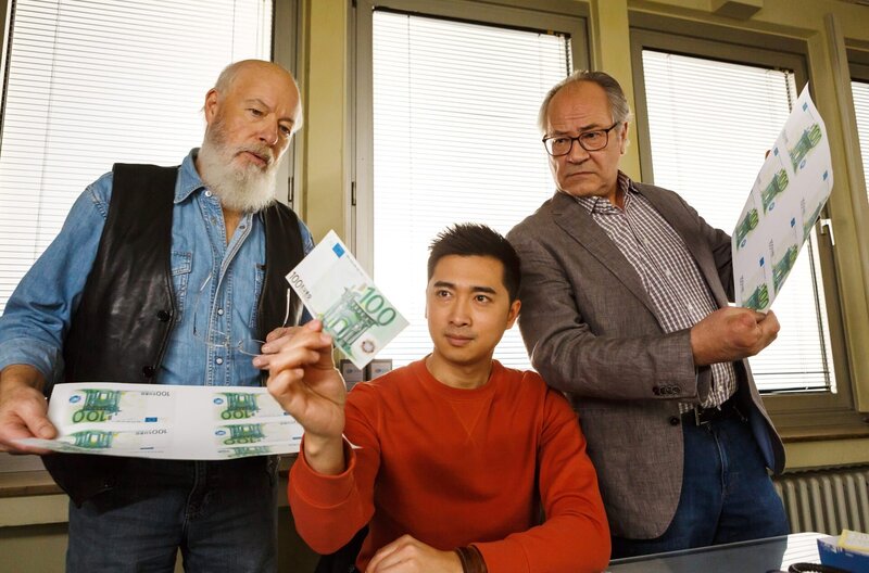 Die Rentnercops Reinhard Bielefelder (Bill Mockridge, l.) und Klaus Schmitz (Hartmut Volle, r.) versuchen sich als Geldfälscher. Hui Ko (Aaron Le, M.) begutachtet das Ergebnis. – Bild: ARD/​Kai Schulz