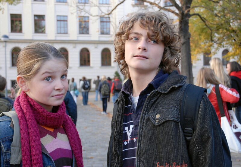 Als Rebecca (Elisabeth Böhm) Paul (Moritz Mack) mit einem Kuss auf den Mund begrüßt, werden die beiden durch ein lautes Hupen gestört – Rebeccas Vater fährt auf den Schulhof. – Bild: BR/​ARD/​Christa Köfer