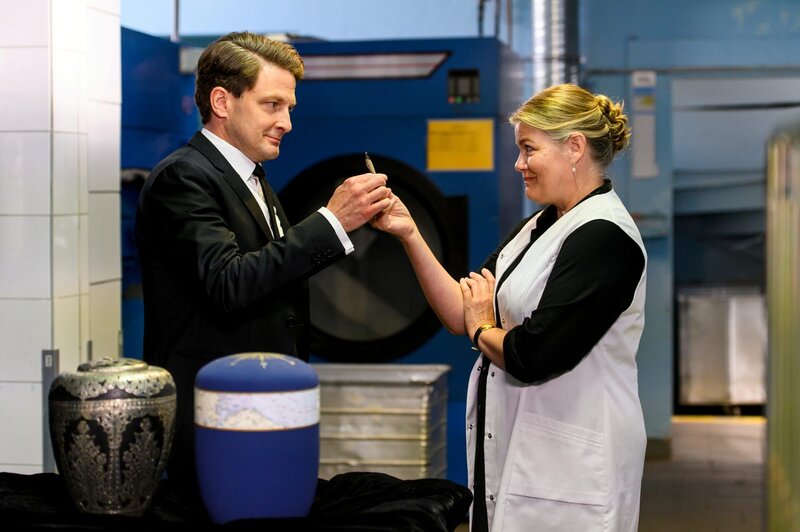 Bestatter Wolfgang Habedank (Holger Stockhaus) bietet der Witwe Frida Van Wieren (Birge Schade) einen Joint als Geste des Trostes an. – Bild: Marius Becker /​ ZDF Enterprises GmbH