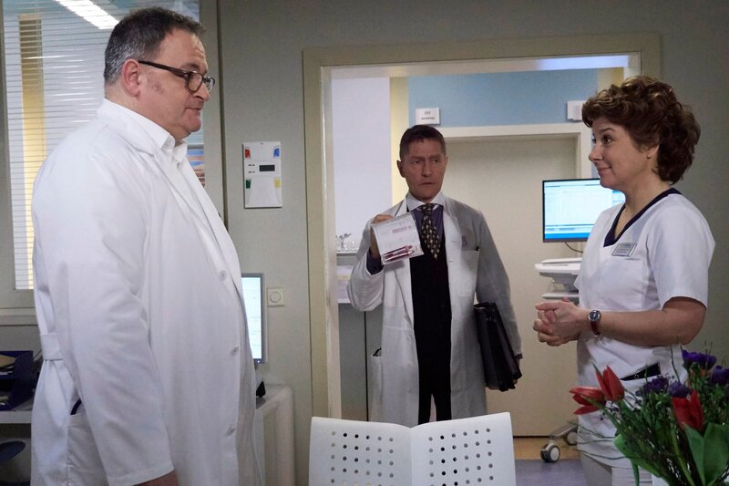 Hans-Peter Brenner (Michael Trischan, li.) soll das erste Mal auf der Visite die Patienten vorstellen. Er ist so aufgeregt, dass er vor Schwester Ulrike (Anita Vulesica) einen Probevortrag hält. Ausgerechnet Dr. Kaminski (Udo Schenk, mi.) platzt in dieser Situation ins Schwesternzimmer und erkundigt sich, ob neben Brenners Entertainmentprogramm Zeit für einen wichtigen Gang ins Labor bleibt. – Bild: MDR/​Saxonia Media Filmproduktion/​Wernicke