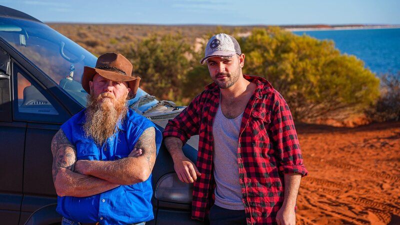 Rod Manning [left] and James „JC“ Caruana [right] standing on red dirt in Shark Bay, in front of the road trip car the ‚Deli‘. – Bild: Warner Bros. Discovery, Inc. or its subsidiaries and affiliates.