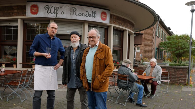 Bielefelder (Bill Mockridge, M.) und Klaus (Hartmut Volle, r.) stehen mit Ulf (Jürgen Hartmann, l.) vor dessen Kneipe (mit Komparsen). – Bild: ARD/​Tom Trambow