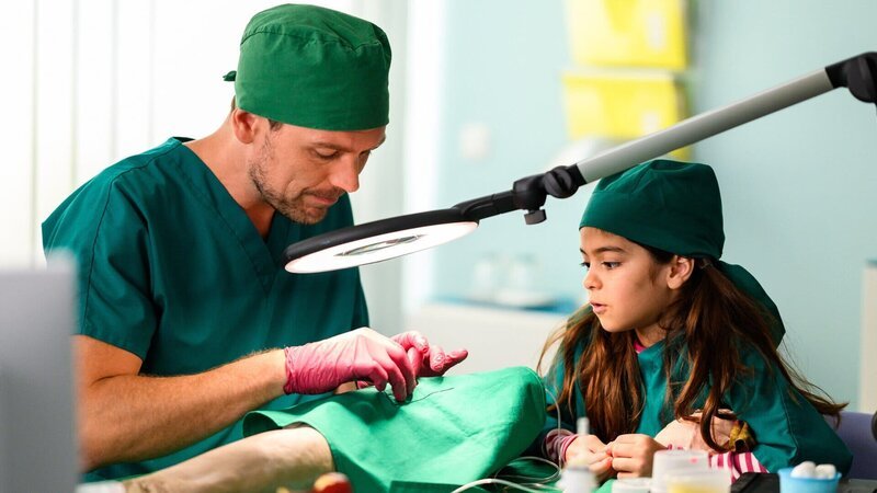 Dr. Walden (Constantin Lücke, r.), nimmt der kleinen Jonna (Soraya Maria Efe, l.) die Angst, dass ihrer Mutter bei der OP etwas zustoßen könnte, indem ihr alle Schritte mithilfe von Knete erklärt. – Bild: ZDF