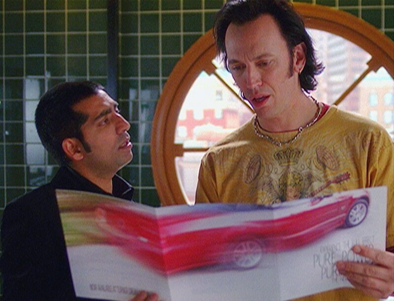 Bug (Ravi Kapoor, l.) platzt fast vor Stolz über sein neues Auto. Er zeigt seinem Kollegen Nigel (Steve Valentine) die bunten Prospekte. – Bild: RTL /​ NBC Universal