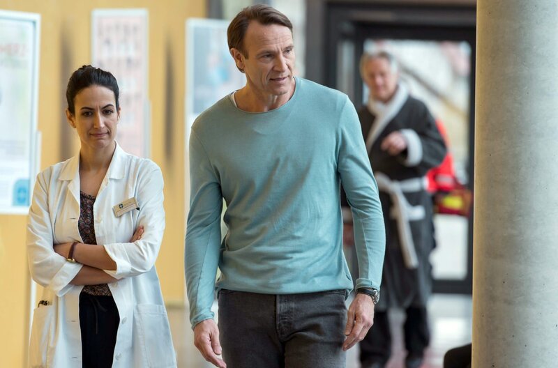 Martin Stein (Bernhard Bettermann, r. mit Komparse, h.) und Leyla (Sanam Afrashteh) besprechen sich zum Fall. Martin geht der Zustand des Patienten nah. Auch Leyla bedrückt etwas. – Bild: ARD/​Jens Ulrich Koch