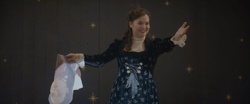 Josie (Yuki Sutton) performt mit der Zauberkraft von Theo und Darius und hat dabei Theo in ein Papierpüppchen verwandelt. – Bild: ZDF/​(c) 2023 Cottonwood Media – ZDF – ZDF Studios